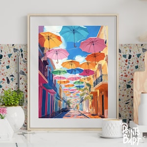 May include: A colourful painting of a street lined with colourful buildings and a canopy of brightly coloured umbrellas overhead. The umbrellas are arranged in a row, creating a tunnel of colour. The street is empty, and the buildings are painted in shades of pink, yellow, and blue.