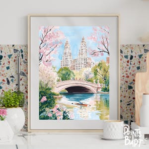 Puede incluir: Una pintura de acuarela de un puente en Central Park, Nueva York. El puente es rosa y blanco y tiene un par de personas caminando por él. Hay edificios altos en el fondo y un bote de remos en el agua.