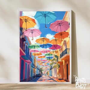May include: A colourful street scene with a row of buildings and a street lined with colourful umbrellas hanging overhead. The umbrellas are in various shades of pink, blue, yellow, orange, and green.