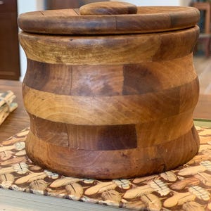 Op de afbeelding: Een houten container met een deksel, gemaakt van meerdere stukken hout, met een natuurlijke houten afwerking.