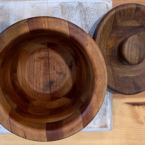 Op de afbeelding: Een houten kom met een deksel, beide gemaakt van meerdere stukken hout. De kom is leeg en het deksel is gesloten.