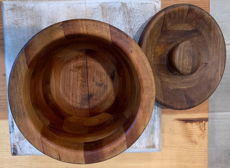 Op de afbeelding: Een houten kom met een deksel, beide gemaakt van meerdere stukken hout. De kom is leeg en het deksel is gesloten.