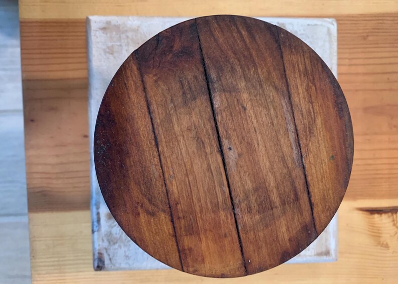 Op de afbeelding: Een ronde houten tafelblad met een donkerbruine vlek. De houtnerf is zichtbaar en er zitten verschillende knopen in het hout.