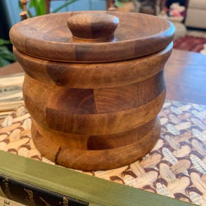 Op de afbeelding: Een houten container met een deksel, gemaakt van meerdere stukken hout, met een natuurlijke houten afwerking.