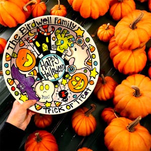May include: A round ceramic plate featuring a hand-painted Halloween theme with a central Happy Halloween text, surrounded by illustrations of a pumpkin, a skull, a bat, a spider, a ghost, and a zombie hand, with The Birdwell Family Trick or Treat text.