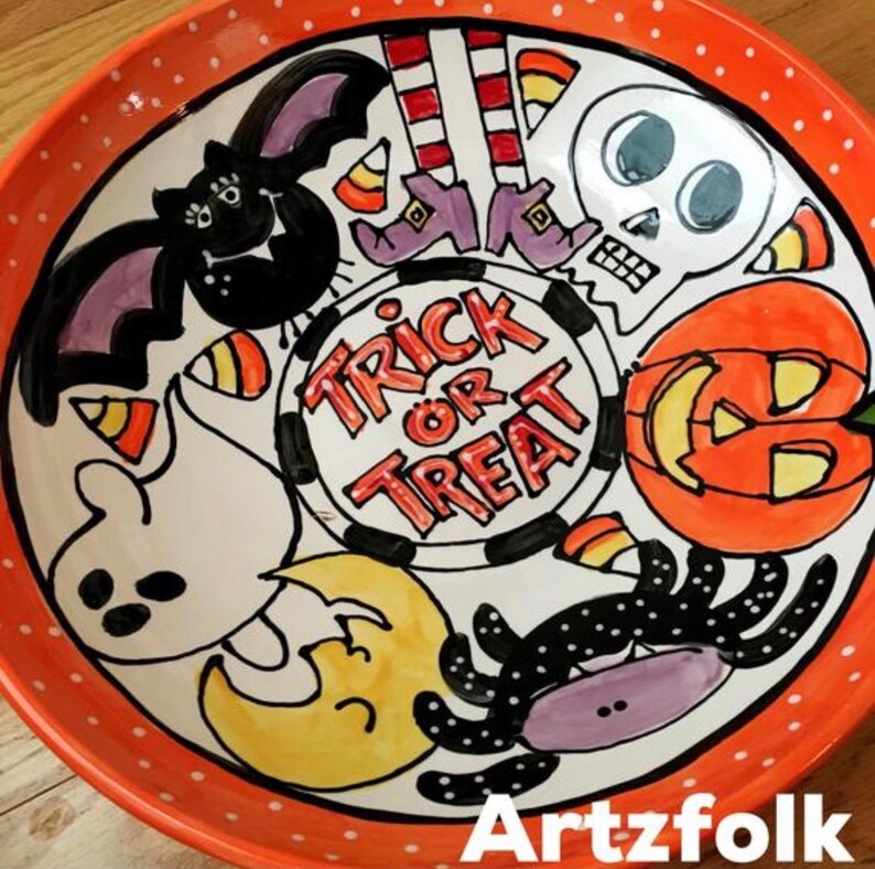 May include: A round ceramic bowl with an orange rim featuring white polka dots. The center displays the text "TRICK OR TREAT" surrounded by hand-painted Halloween illustrations including a black bat, a skull, a pumpkin, a ghost, a spider, and candy corn.