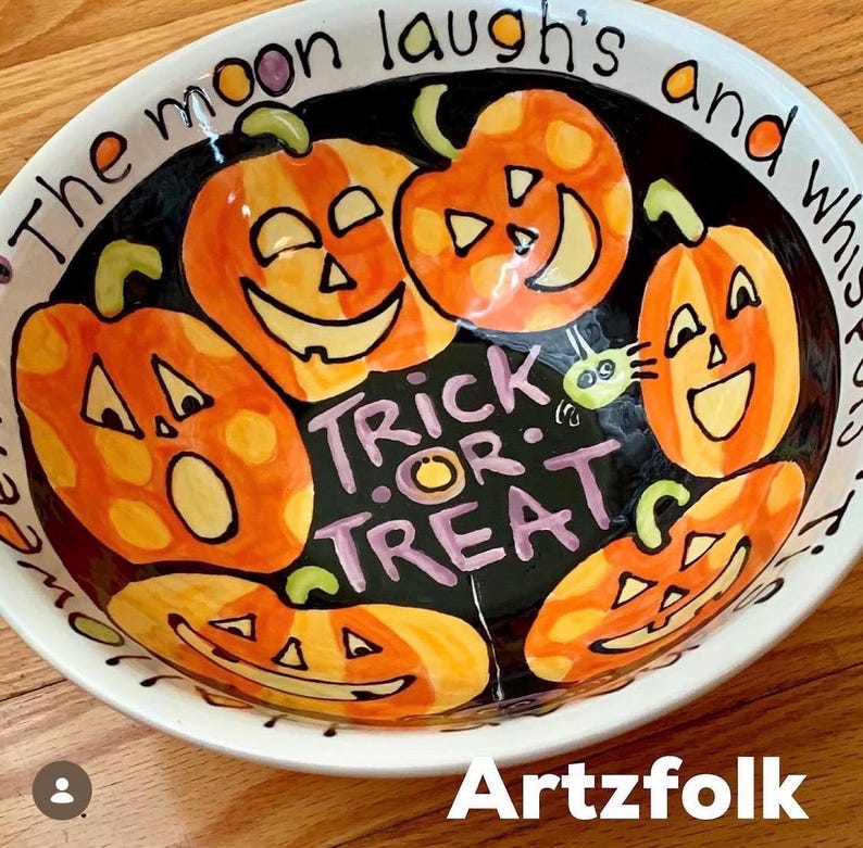 May include: A round ceramic bowl with a black interior featuring five orange jack-o'-lanterns and the purple text "TRICK OR TREAT". The white rim displays the text "The moon laugh's and whispers". The bowl has a glossy finish and hand-painted details.