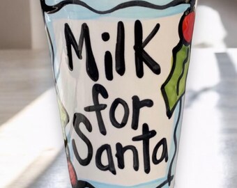 May include: A white ceramic tumbler with the words "Milk for Santa" in black script. The tumbler has a blue wavy border, holly and berry accents, and a black and white checkered rim. Red and green polka dots are also featured.