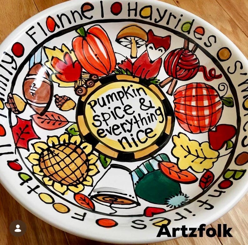 May include: A white ceramic bowl featuring hand-painted autumn illustrations including a pumpkin, fox, sunflower, football, and leaves. The center text reads, "Pumpkin spice & everything nice," while the rim text includes "Flannel," "Hayrides," and "Bonfires."