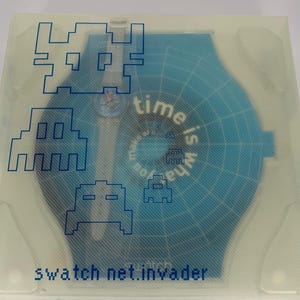 Pu&ograve; includere: Un orologio Swatch nella sua confezione originale. L'orologio &egrave; blu con una cassa blu abbinata. La confezione ha una copertura trasparente con grafica blu di invasori spaziali pixelati e la scritta "time is what you make of it". Il testo "swatch net.invader" &egrave; anch'esso visibile.