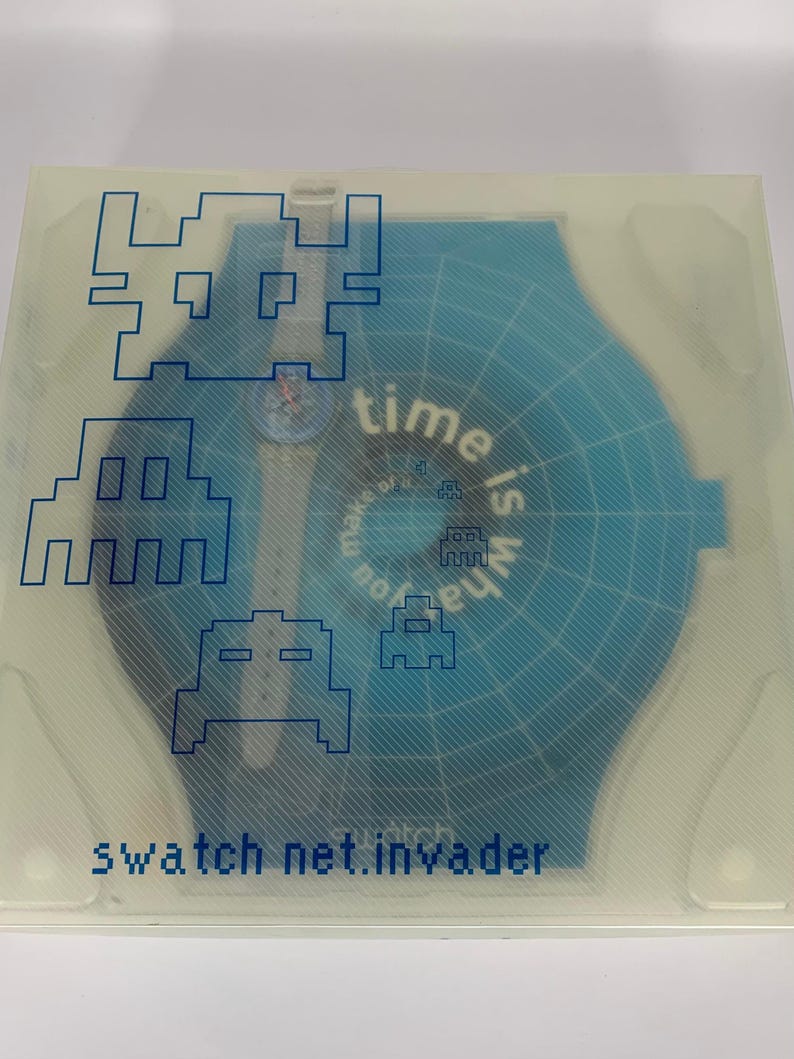 Pu&ograve; includere: Un orologio Swatch nella sua confezione originale. L'orologio &egrave; blu con una cassa blu abbinata. La confezione ha una copertura trasparente con grafica blu di invasori spaziali pixelati e la scritta "time is what you make of it". Il testo "swatch net.invader" &egrave; anch'esso visibile.