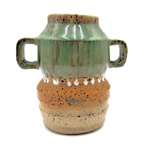 May include: A ceramic vase with two handles, featuring a glossy green upper section and a speckled orange and beige lower section. A row of white drip-like glaze accents separates the green and orange areas, creating a distinct visual contrast.