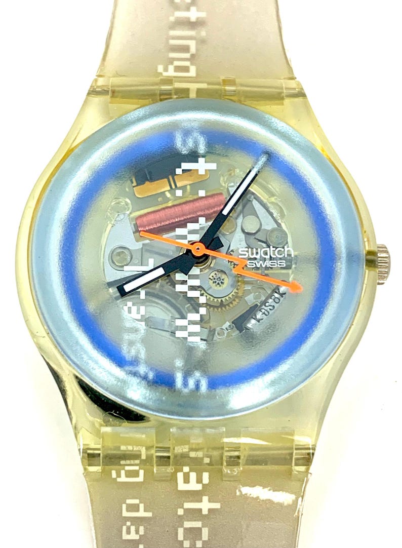 Pu&ograve; includere: Un orologio Swatch Swiss trasparente con un anello del quadrante blu chiaro e lancette arancioni. Il quadrante dell'orologio mostra il meccanismo interno. Il cinturino dell'orologio riporta le parole "setting" e "date".