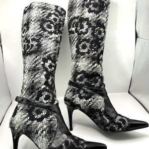 May include: A pair of knee-high boots with a black, white, and gray patterned textile upper. The boots have black leather accents, pointed toes, and stiletto heels. The heels are approximately 4 inches tall.