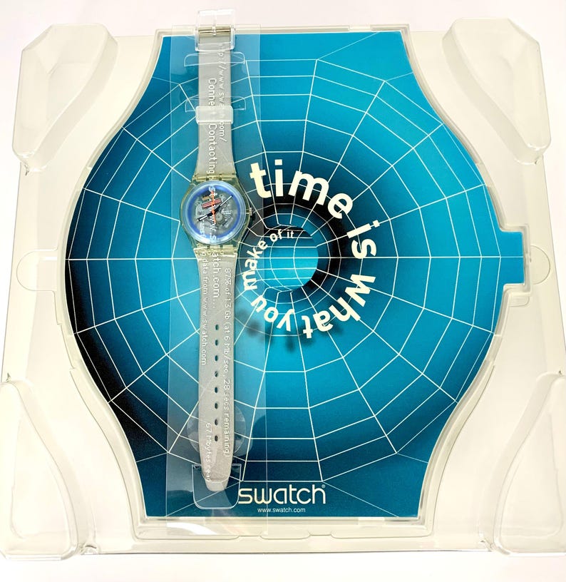 Pu&ograve; includere: Un orologio Swatch con cinturino trasparente e quadrante blu e rosso, esposto nella sua confezione originale. L'orologio &egrave; posto su uno sfondo blu con la scritta "time is what you make of it". Il logo Swatch &egrave; visibile.