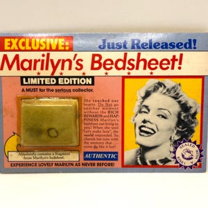 May include: A collectible card with the text "Marilyn's Bedsheet!" and a photo of Marilyn Monroe. The card is labeled "Exclusive" and "Limited Edition." It contains a fragment from Marilyn's bedsheet. The card is sealed with a kiss.