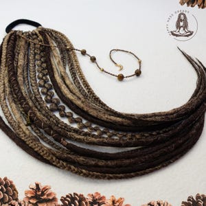 May include: A set of brown, blonde, and light brown synthetic dreadlocks with a brown elastic hair tie and a beaded necklace with a crescent moon charm.