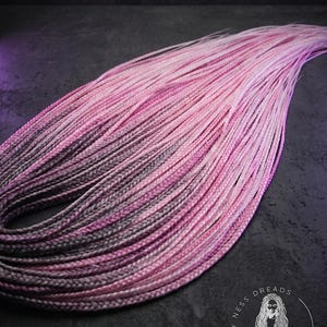 May include: Pink and grey braided synthetic hair extensions. The hair is arranged in a wavy pattern, with a gradient effect from light pink to dark grey. The Happy Ness Dreads logo is visible in the bottom right corner.