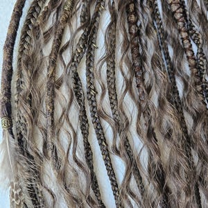 Handcrafted synthetic dreads extensions with intricate braided dreads and curls. Decorated with feathers, copper charms, beads, threads, this ponytail is easy to attach and remove, offering a hassle-free alternative to permanent dreads installations.