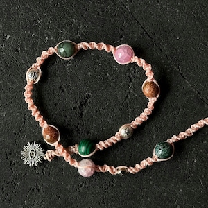 May include: A pink and brown braided cord bracelet with various colored gemstone beads, including green, pink, and brown.