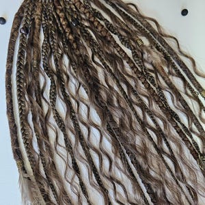 Hair on elastic band with auburn braids, curls, and dreadlocks, decorated with feathers, copper charms, beads, and threads. This handmade piece is perfect for bohemian hairstyles, adding texture and style effortlessly.
