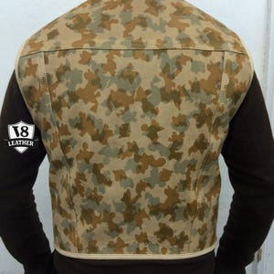 May include: Camouflage pattern leather vest in shades of tan, brown, and green. The vest has a high collar and a cream-colored trim. The back of the vest is visible, showcasing the camouflage design. The vest is a stylish outerwear piece.
