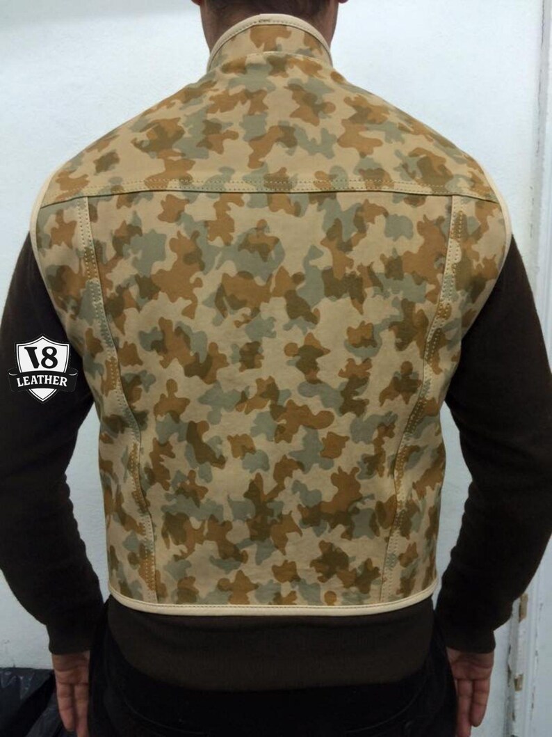 May include: Camouflage pattern leather vest in shades of tan, brown, and green. The vest has a high collar and a cream-colored trim. The back of the vest is visible, showcasing the camouflage design. The vest is a stylish outerwear piece.