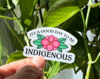 May include: A white sticker with a pink flower and green leaves. The sticker says "It's a good day to be Indigenous".