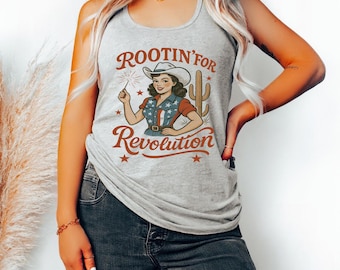 May include: Heather grey vest top featuring a cowgirl graphic with a sparkler, the text "Rootin' for Revolution", and a cactus. The top is worn with blue jeans. The words "Heather Grey" are at the bottom.