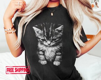 May include: Black t-shirt featuring a grayscale image of a kitten. The kitten is depicted with a detailed, realistic style. The t-shirt has a classic crew neck design.