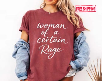 May include: A maroon t-shirt with the text "woman of a certain Rage" in white script. The shirt has rolled-up sleeves and is worn with a denim jacket. The overall style is casual and comfortable.