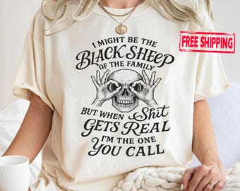 May include: Cream-coloured t-shirt with a black skull graphic and the text "I MIGHT BE THE BLACK SHEEP OF THE FAMILY BUT WHEN SHIT GETS REAL I'M THE ONE YOU CALL." The shirt has short sleeves.
