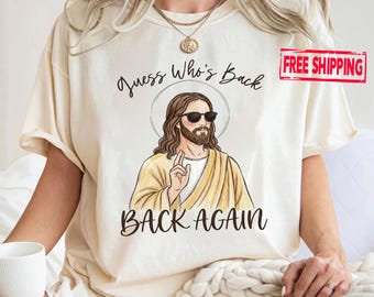 May include: Cream-colored t-shirt featuring a graphic of Jesus wearing sunglasses, with the text "Guess Who's Back" above and "BACK AGAIN" below. The design is a humorous take on religious imagery.