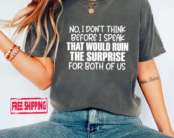 May include: A charcoal grey short-sleeve t-shirt featuring white text that reads: NO, I DON'T THINK BEFORE I SPEAK THAT WOULD RUIN THE SURPRISE FOR BOTH OF US. The shirt has a crew neckline and a relaxed fit, paired with blue denim jeans.