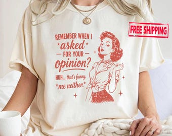May include: A cream-colored t-shirt featuring red text that reads, "REMEMBER WHEN I asked FOR YOUR opinion? HUH... that's funny, *me neither*." Next to the text is a red line-art illustration of a person with wavy hair wearing a tied shirt.