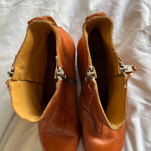 Puede incluir: Un par de botines de cuero marr&oacute;n con punta puntiaguda y cremalleras laterales. Las botas tienen un aspecto desgastado y est&aacute;n hechas de cuero suave y flexible.