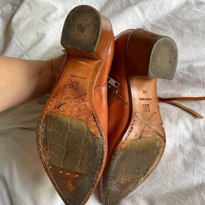 Puede incluir: Un par de botines de cuero marr&oacute;n con punta puntiaguda y cremallera lateral. Las botas tienen un peque&ntilde;o tac&oacute;n de bloque y las suelas est&aacute;n desgastadas. El texto "40" y "MADE IN ITALY" es visible en las suelas.