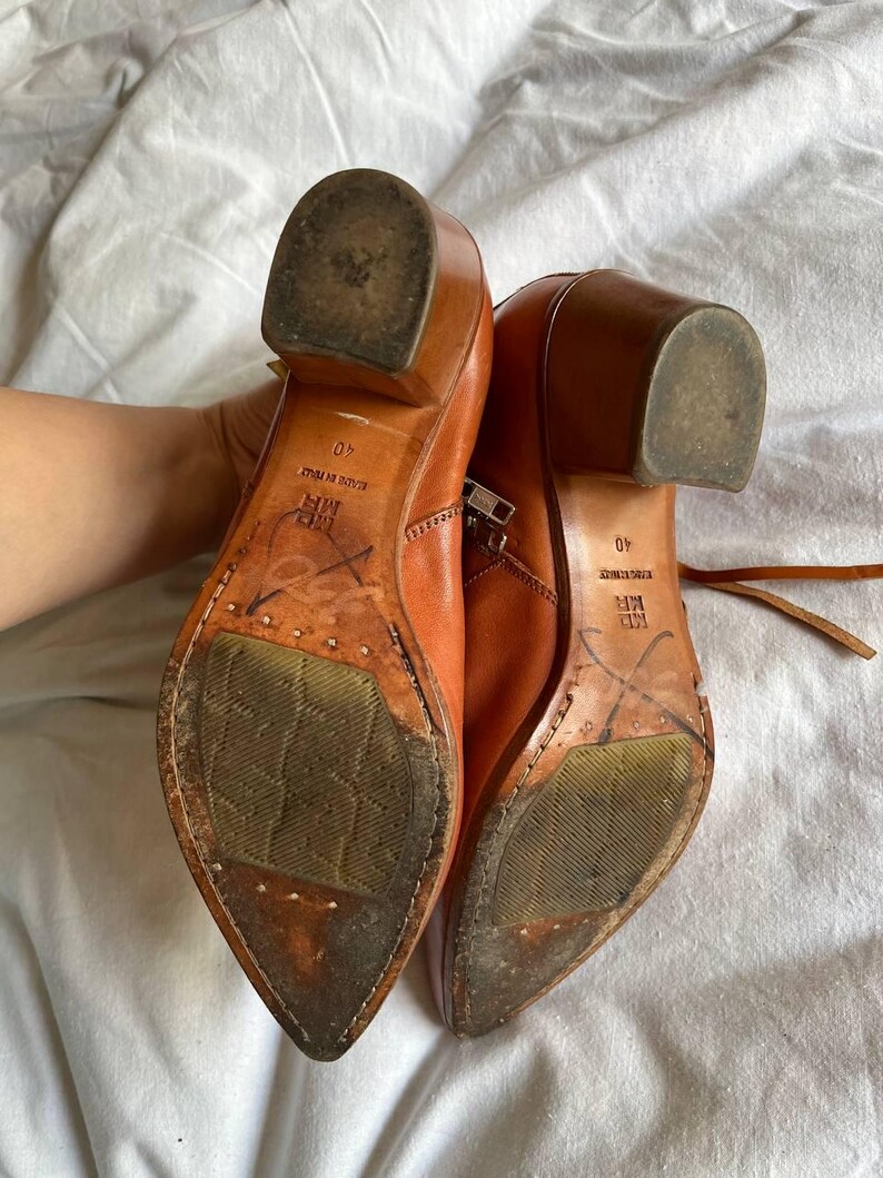 Puede incluir: Un par de botines de cuero marr&oacute;n con punta puntiaguda y cremallera lateral. Las botas tienen un peque&ntilde;o tac&oacute;n de bloque y las suelas est&aacute;n desgastadas. El texto "40" y "MADE IN ITALY" es visible en las suelas.