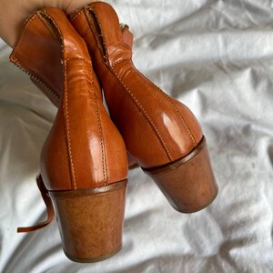 Puede incluir: Un par de botines de cuero marr&oacute;n con tac&oacute;n grueso. Las botas tienen una cremallera en el interior de cada bota y una correa alrededor del tobillo.