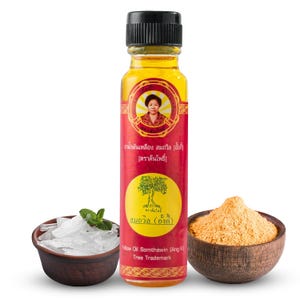 May include: A small bottle of yellow oil with a red label that says "Yelow Oil Somthawin (Ang K) Tree Trademark". The label also features a picture of a woman and a tree. There is a bowl of ice cubes and a bowl of yellow powder in the background.