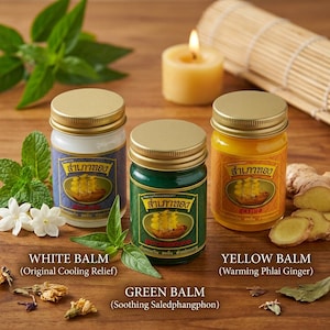 Könnte beinhalten: Drei Glasdöschen mit goldenen Deckeln, die weißen, grünen und gelben Balsam enthalten. Jedes Döschen hat ein Etikett mit einer goldenen Schiff-Illustration und thailändischem Text. Der weiße Balsam ist Original Cooling Relief, der grüne Saledphangphon und der gelbe Warming Phlai Ginger.