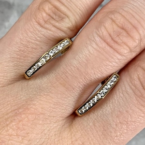 May include: A pair of gold-coloured earrings, each with a line of small, clear gemstones. The earrings are rectangular with rounded edges. The gemstones are set close together, creating a sparkling effect.