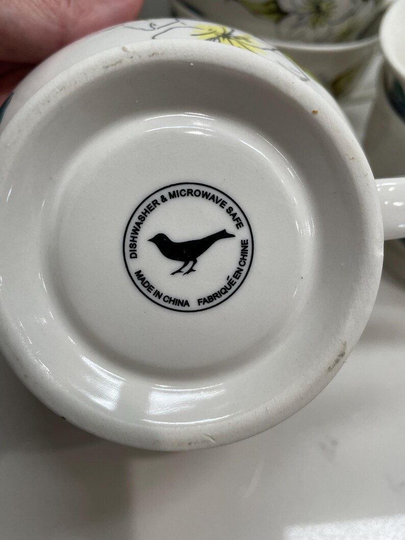 Puede incluir: Base de taza de cer&aacute;mica blanca con una silueta de p&aacute;jaro negro dentro de un c&iacute;rculo que dice "Dishwasher & Microwave Safe" y "Made in China Fabriqu&eacute; en Chine".