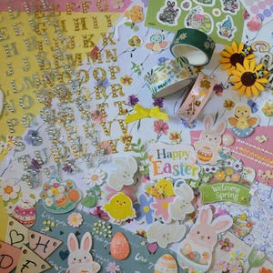 May include: A colorful assortment of Easter-themed craft supplies. The image includes stickers, decorative tape, and embellishments featuring bunnies, eggs, flowers, and the text "Happy Easter" and "Welcome Spring". There are also alphabet stickers and floral patterned paper.