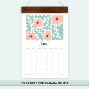 May include: A June wall calendar with a floral design. Pink flowers with blue centres and light green leaves adorn the top. The word "June" is printed in black. The calendar is held by a dark brown wooden bar.