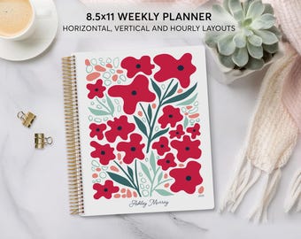 May include: A white weekly planner with a gold coil binding. The cover features a floral design with red flowers and green leaves on a white background. The text "8.5x11 WEEKLY PLANNER" is at the top of the cover. The text "HORIZONTAL, VERTICAL AND HOURLY LAYOUTS" is below the planner title. The planner is personalized with the name "Ashley Murray" and the year "2023".