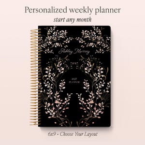 May include: A black weekly planner with gold spiral binding, featuring a delicate botanical illustration of branches with pink and white leaves. The cover displays the text Personalized weekly planner, start any month, Ashley Murray, 2027 PLANNER, and 6x9.