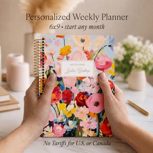May include: A spiral-bound weekly planner featuring a vibrant, painterly floral pattern in shades of pink, red, yellow, and blue on a light blue background. A central white rectangular label displays the text 2027 PLANNER and Julia Bishop.