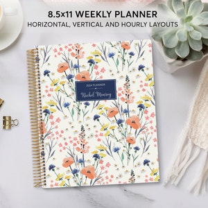 May include: A floral patterned weekly planner with a gold coil binding. The cover features a watercolor design of pink, orange, yellow, and blue flowers on a white background. The planner is labeled "2024 Planner" and "Rachel Murray".