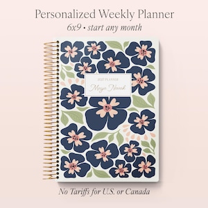 May include: A personalized weekly planner with a floral design. The cover features navy blue flowers with pink centers and green leaves. The planner is 6x9 inches and has a gold spiral binding. The text "Personalized Weekly Planner" and "Maya Novak" are visible.